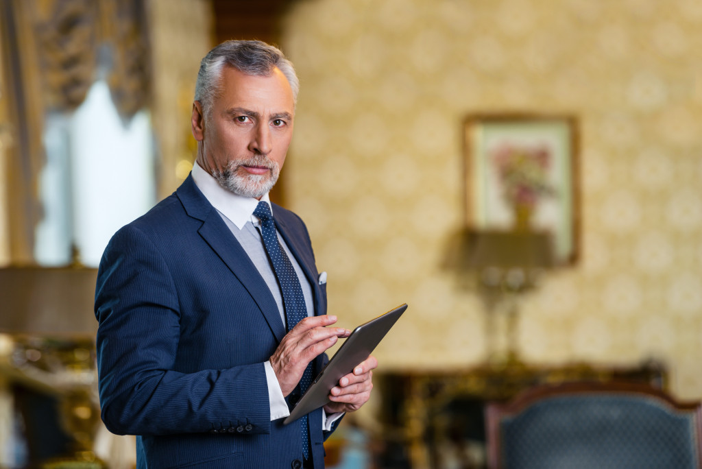 a serious senior businessman holding a tablet on a hotel
