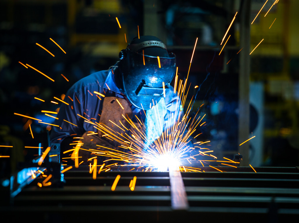 Bright sparks erupt in front of a welder wearing a welding mask, apron, and gloves