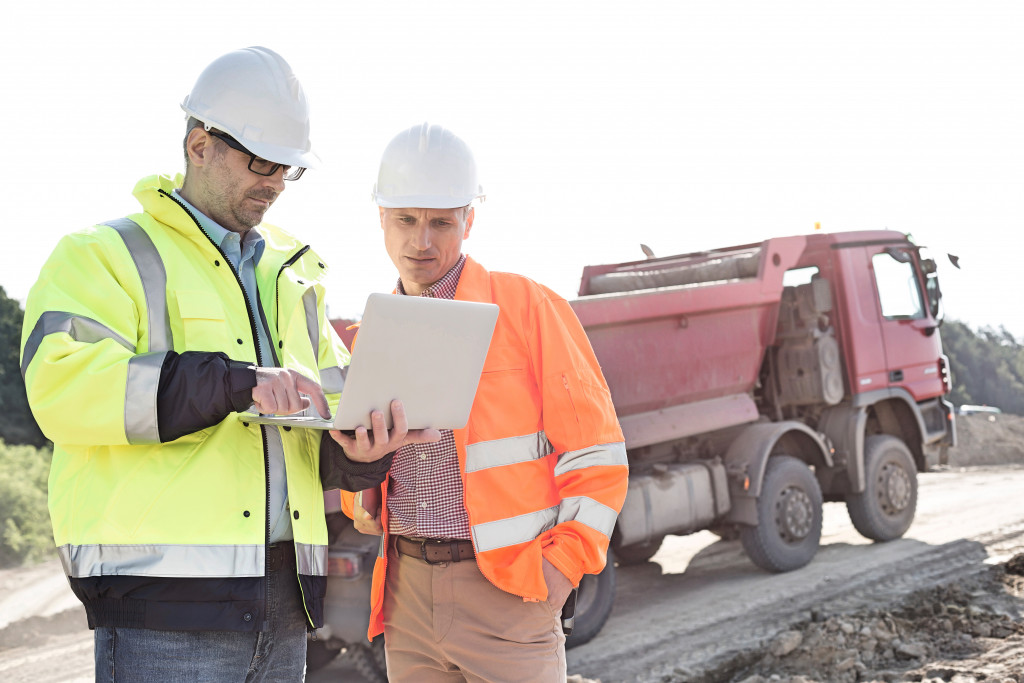 Two engineers using a laptop on a construction site with a truck
