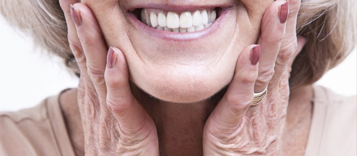 elder woman with wrinkles touching her cheeks while smiling