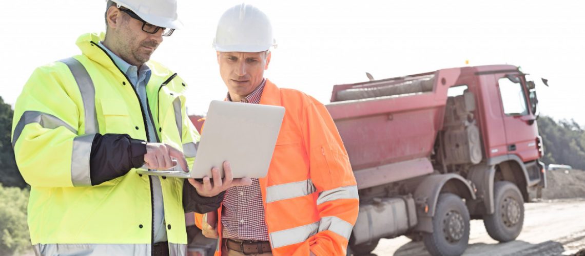 Two engineers using a laptop on a construction site with a truck