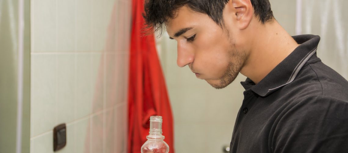 Head and Shoulders Close Up of Attractive Young Man with Dark Hair Rinsing with Mouth Wash in Bathroom as part of Morning Grooming Routine