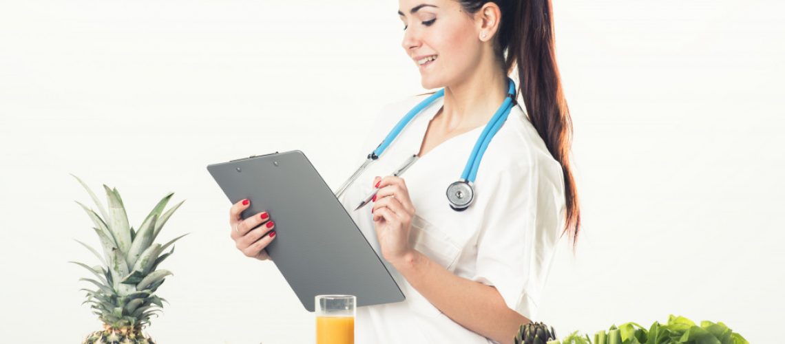medical personnel wearing stethoscope in her neck surrounded by fruits and vegetables