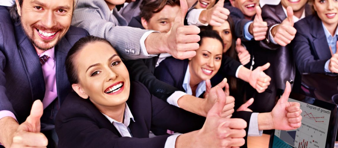 A group of employees in business attire are smiling and showing their thumbs up